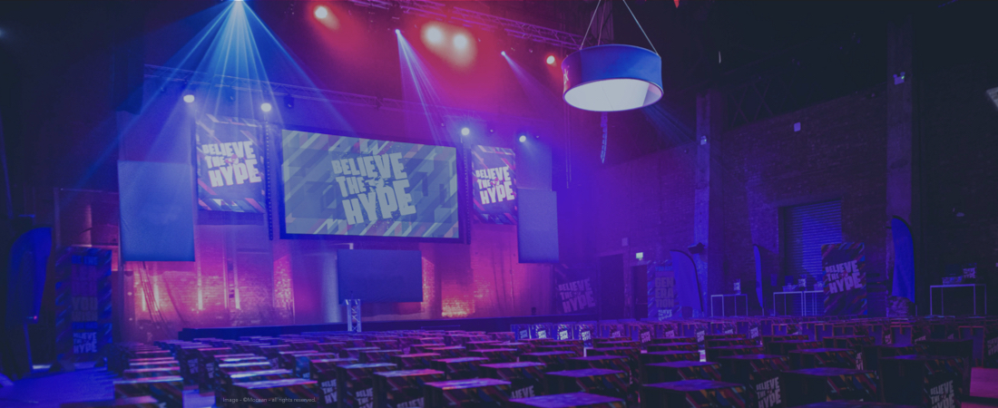 Conference stage set at a corporate event with event theming on screens and sustainable seating.