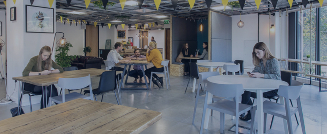 A co-working space with people sat on tables working and engaging with each other.